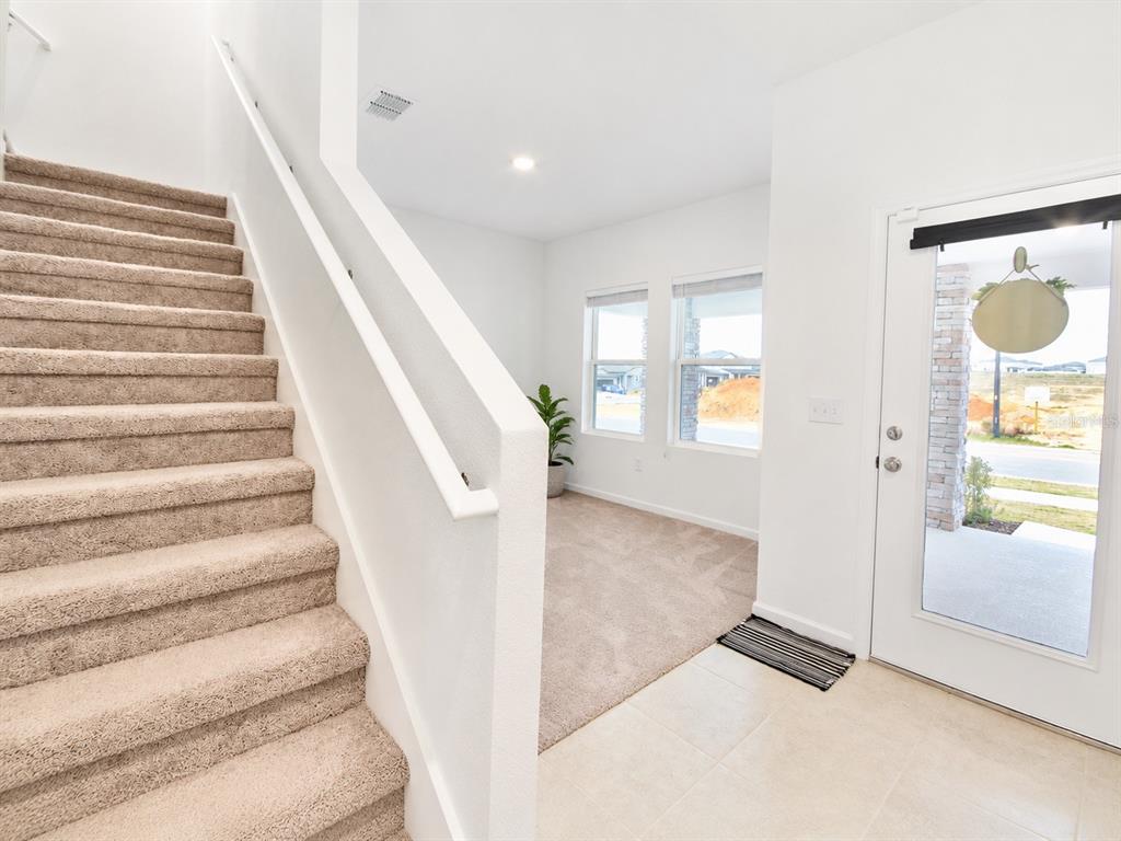 A carpeted staircase leads upward next to a carpeted entryway with a glass-paneled front door — 2150 GOLD DUST DRIVE, CLERMONT, FL