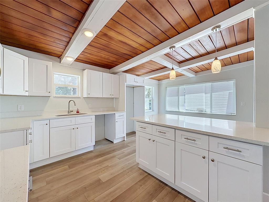 A kitchen features white cabinetry, quartz countertops, wood-plank flooring, and a wood-paneled beamed ceiling — 14339 RICE ROAD, HUDSON, FL