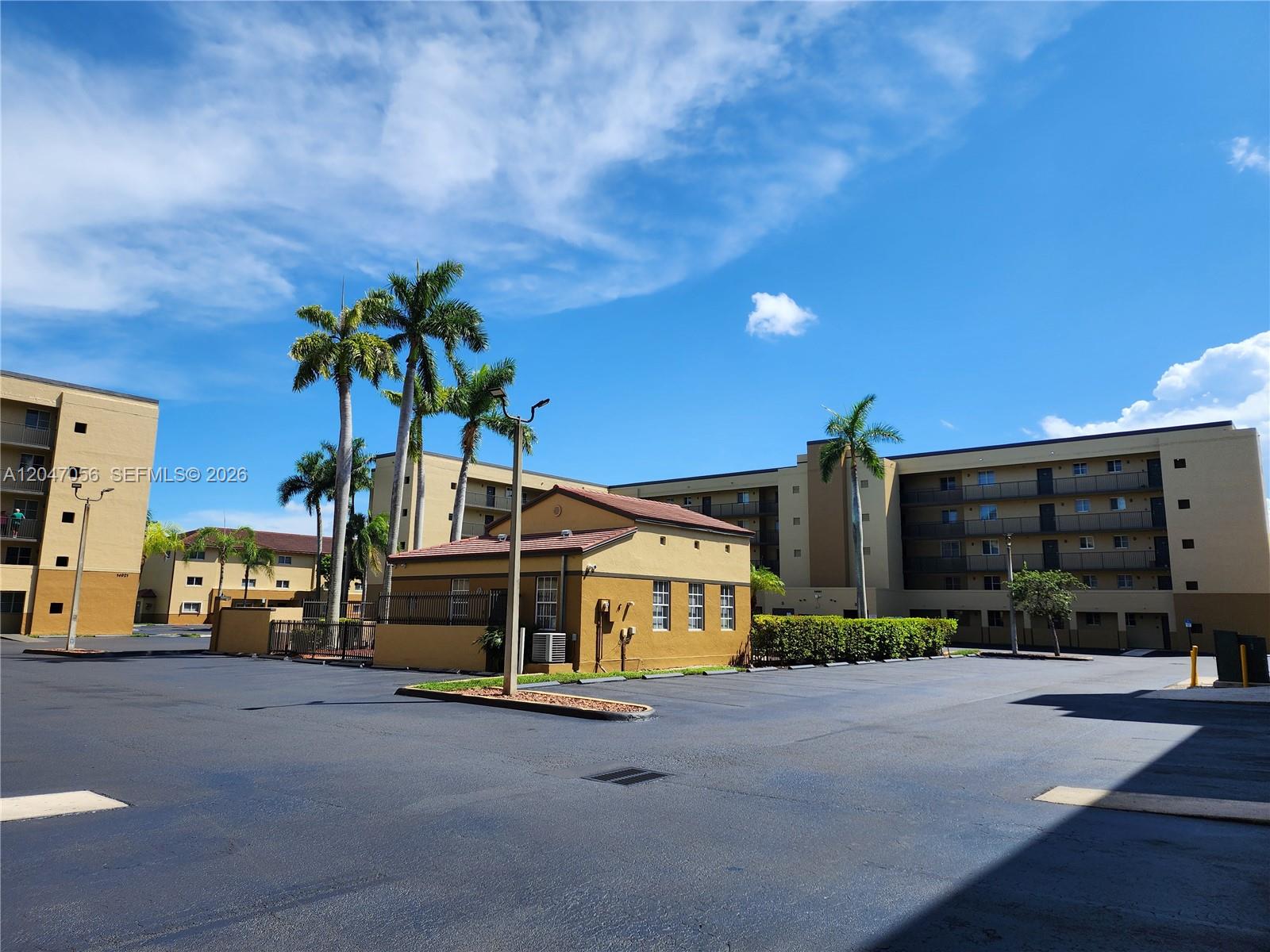 An exterior view shows a parking lot in front of multi-story apartment buildings and palm trees — 14901 SW 82nd Ter # 103, Miami FL 33193, MIAMI, FL