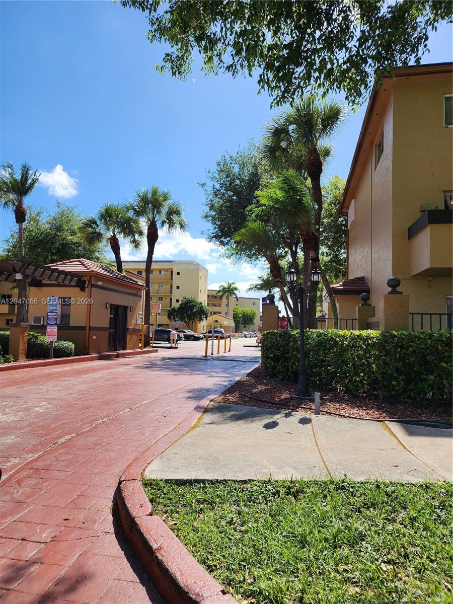 A gated entrance with a red paved driveway leads to multi-story apartment buildings — 14901 SW 82nd Ter # 103, Miami FL 33193, MIAMI, FL