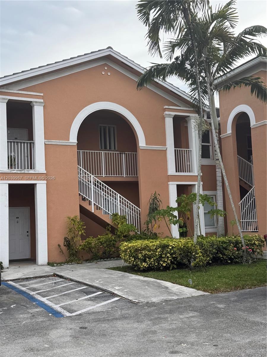 An exterior view of a two-story peach-colored apartment building with white trim and stairs — 7070 NW 177th St # 10, Hialeah FL 33015, HIALEAH, FL