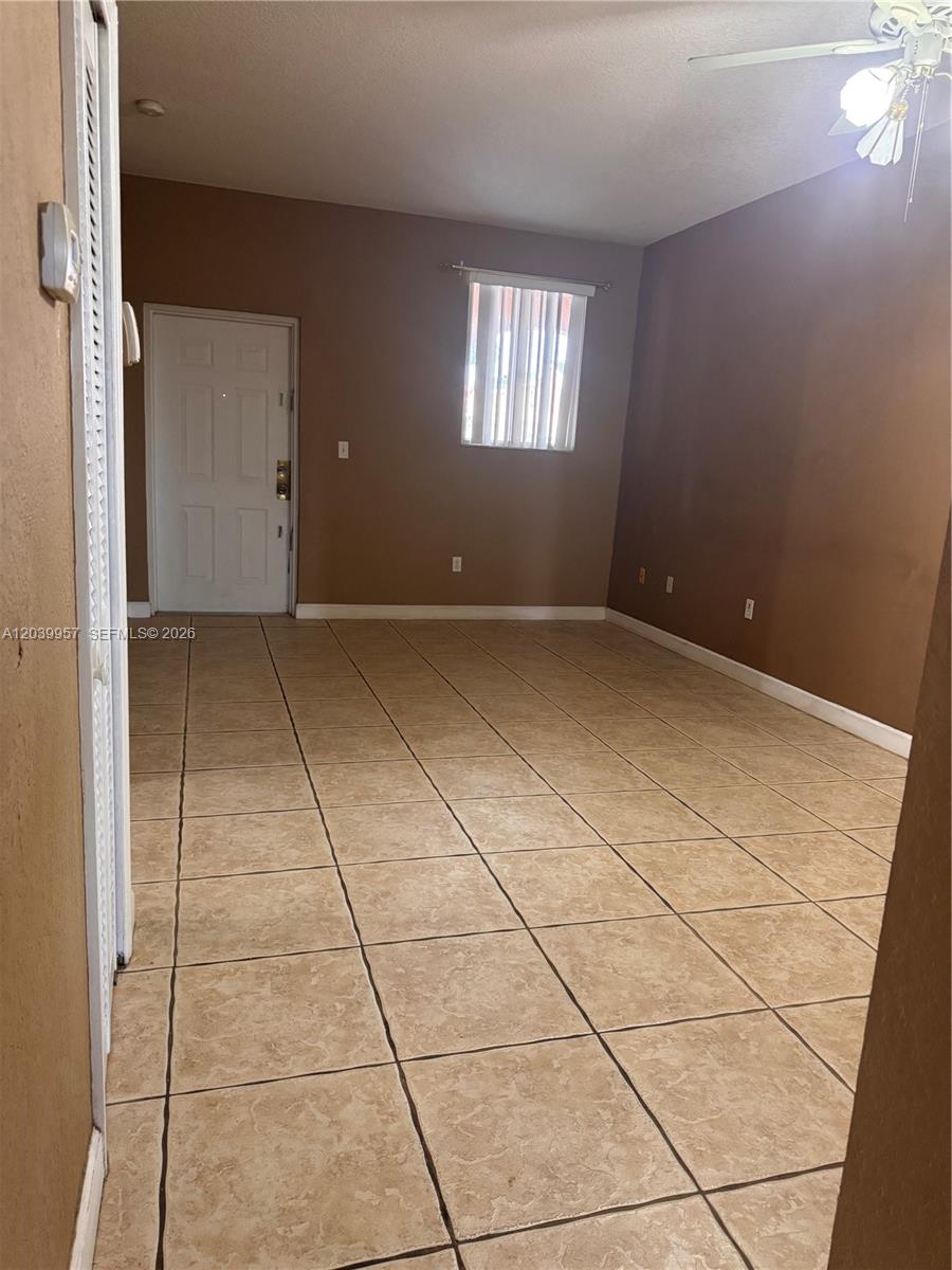 An empty room features tan tile flooring, brown walls, a ceiling fan, and a white door — 7070 NW 177th St # 10, Hialeah FL 33015, HIALEAH, FL