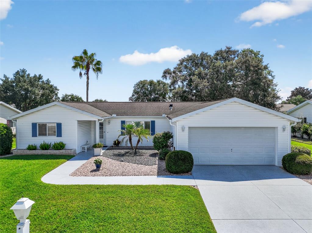 A white, single-story house with a two-car garage, blue shutters, and a landscaped front yard — 17551 SE 96TH COURT, SUMMERFIELD, FL