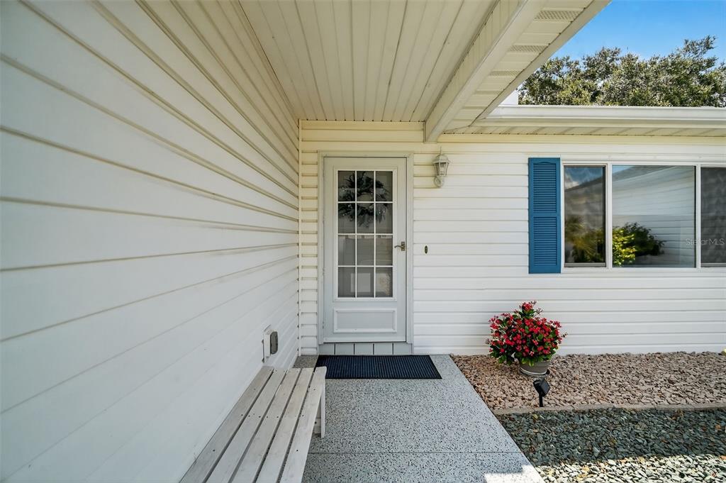 A white front door with a glass panel sits on a porch with a bench — 17551 SE 96TH COURT, SUMMERFIELD, FL