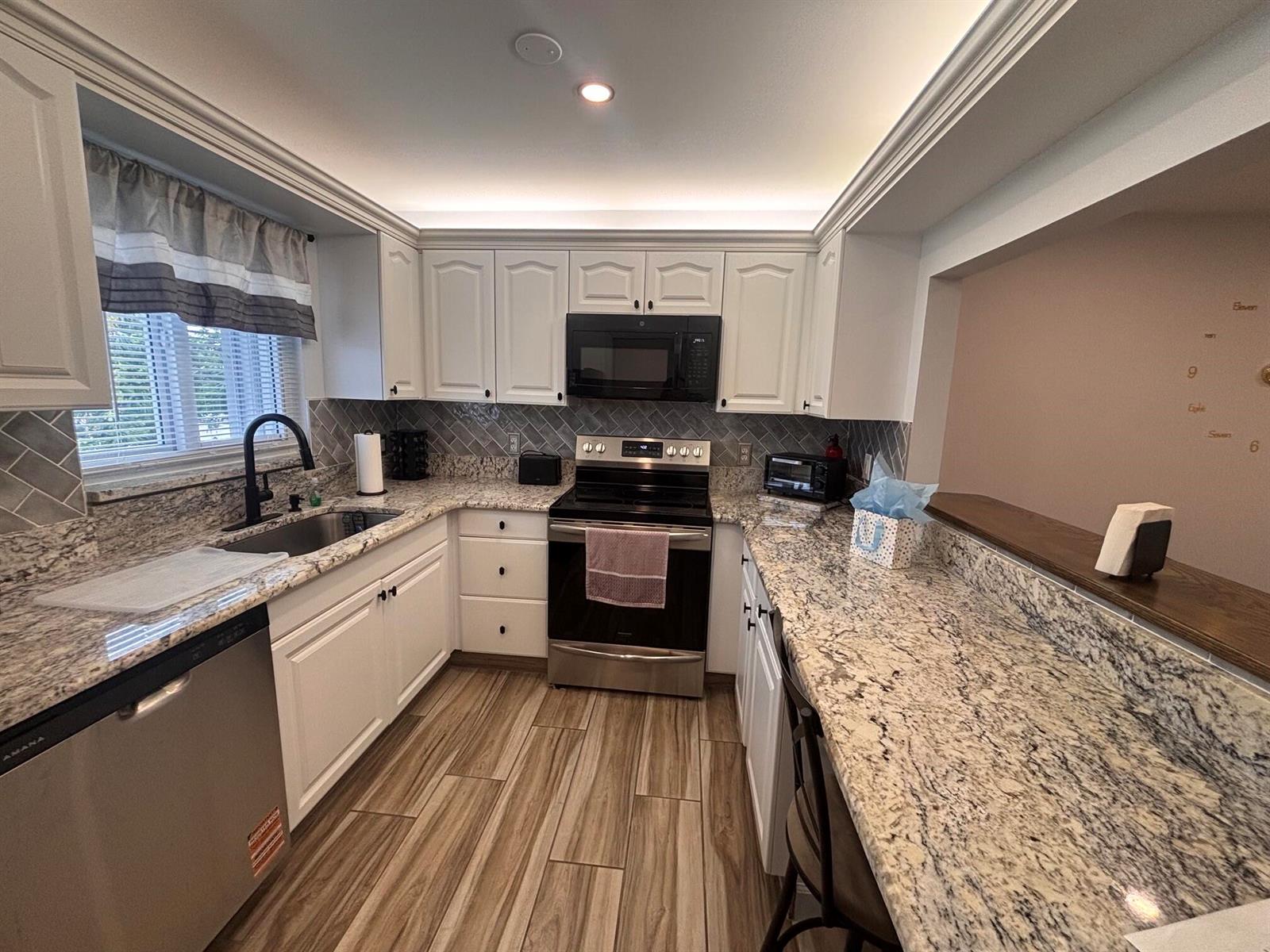 A kitchen features white cabinetry, granite countertops, stainless steel appliances, and wood-look tile flooring — 2950 SE Ocean Boulevard # 5, Stuart FL 34996, STUART, FL