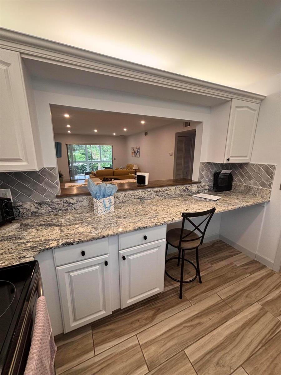 A kitchen features white cabinets, granite countertops, a pass-through window, and wood-look tile flooring — 2950 SE Ocean Boulevard # 5, Stuart FL 34996, STUART, FL