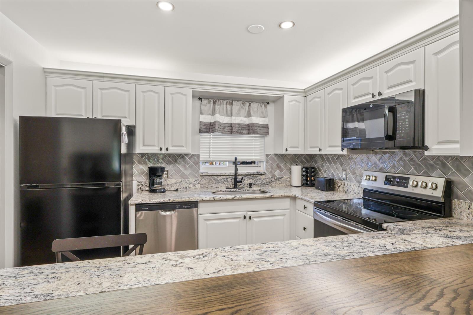 A kitchen features white cabinets, granite countertops, a gray tile backsplash, and black appliances — 2950 SE Ocean Boulevard # 5, Stuart FL 34996, STUART, FL