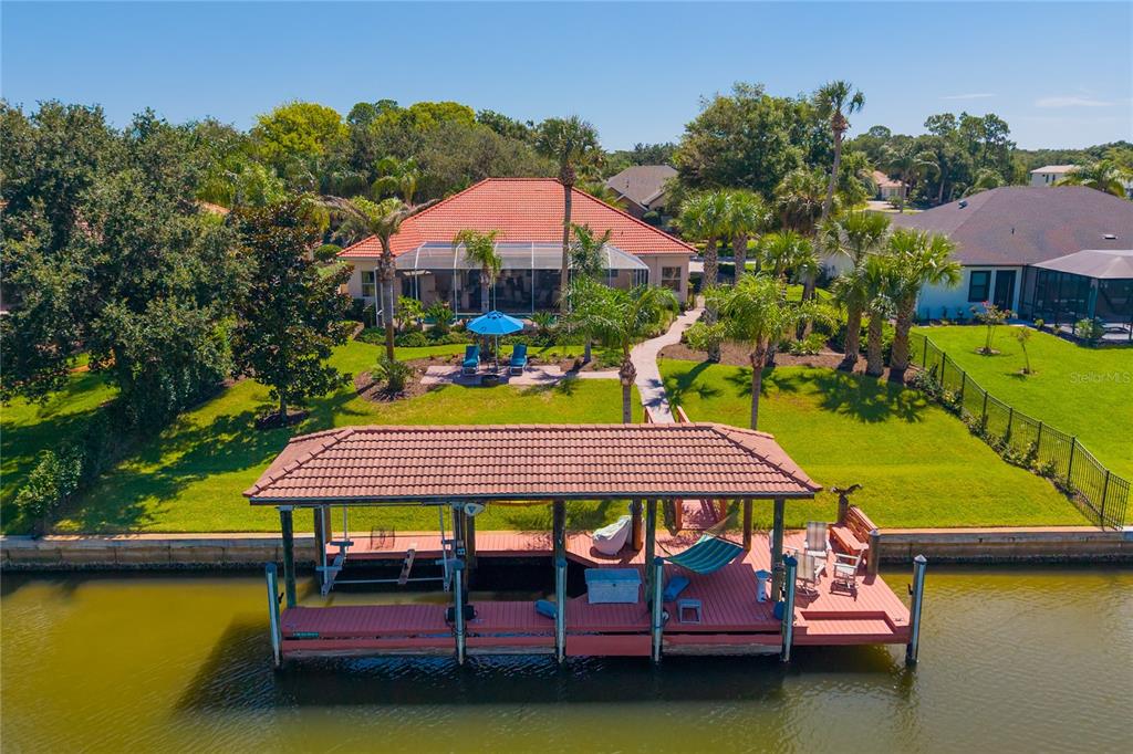 An aerial view shows a waterfront house with a tiled roof, pool cage, and dock — 8 OLD OAK DRIVE N, PALM COAST, FL