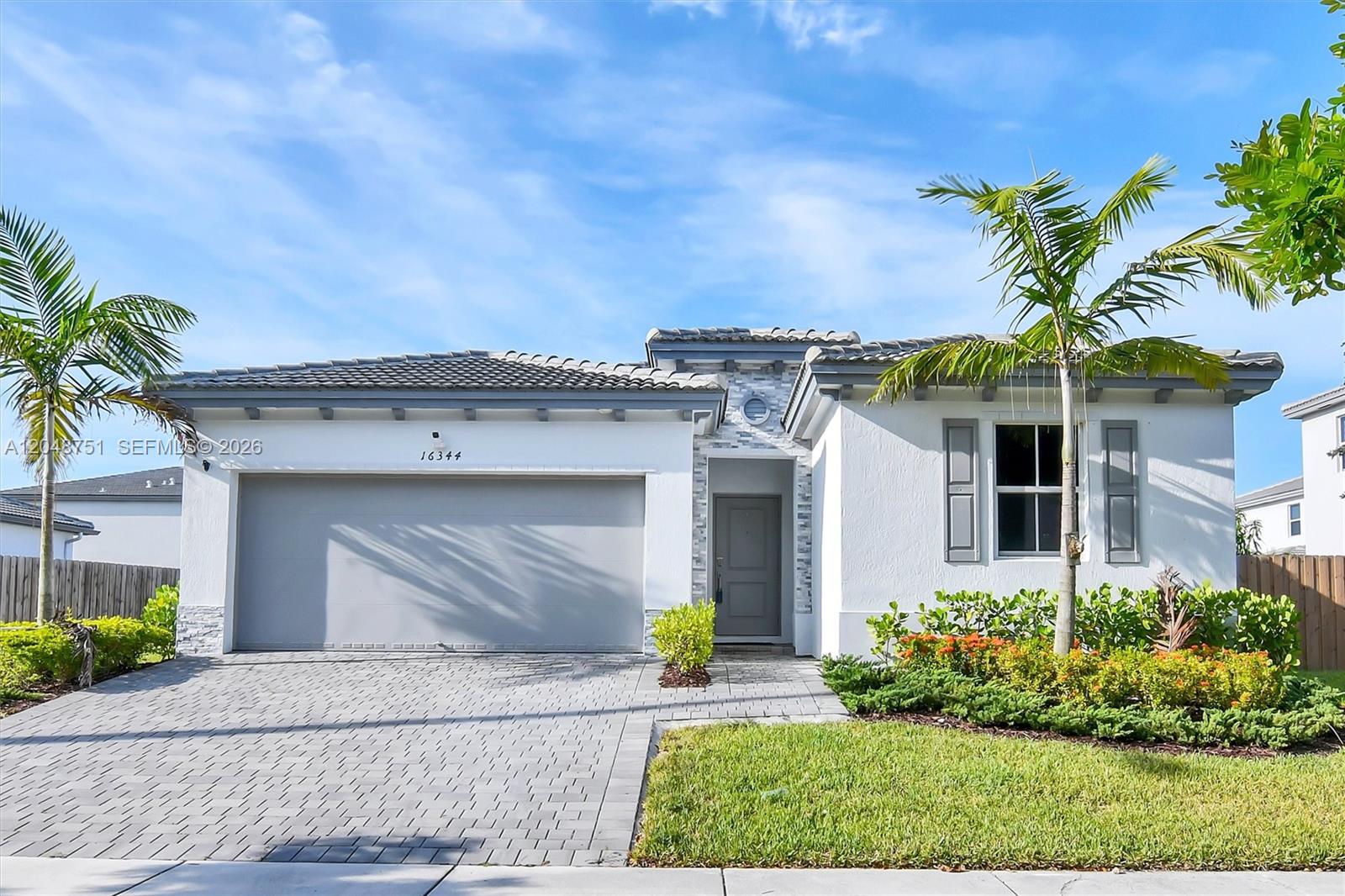 A single-story house features a two-car garage, a paved driveway, and palm trees — 16344 SW 290th St, Homestead FL 33033, HOMESTEAD, FL