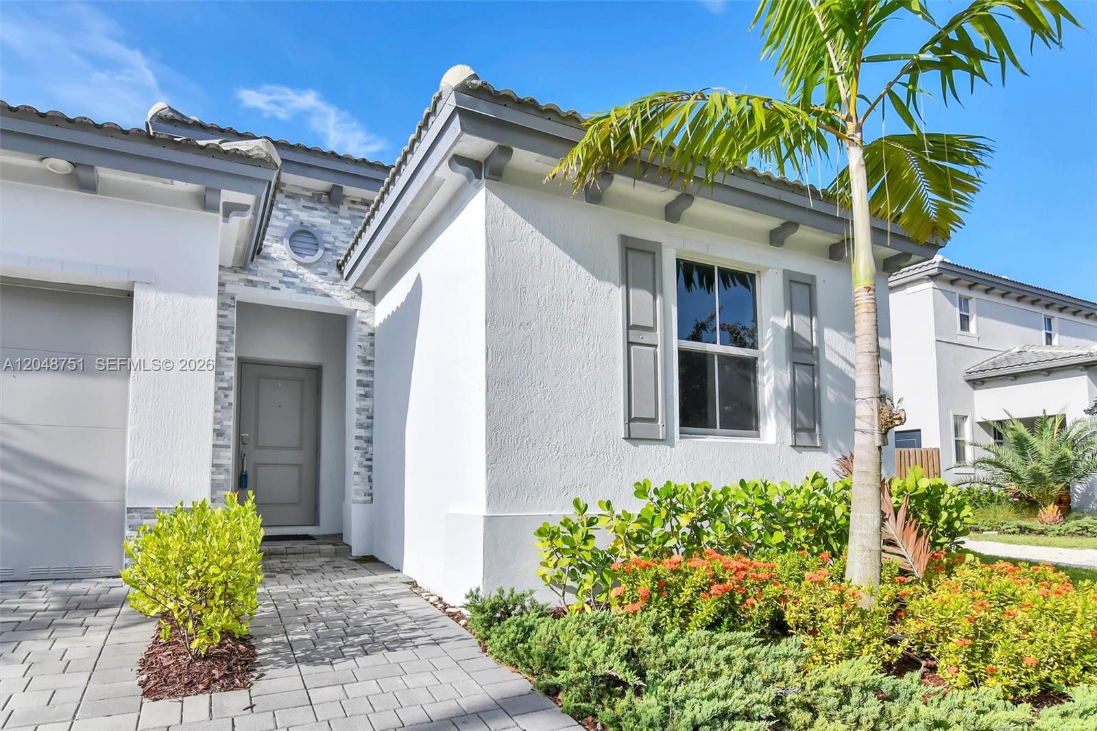 The exterior of a white house features a gray front door, shutters, and landscaping — 16344 SW 290th St, Homestead FL 33033, HOMESTEAD, FL