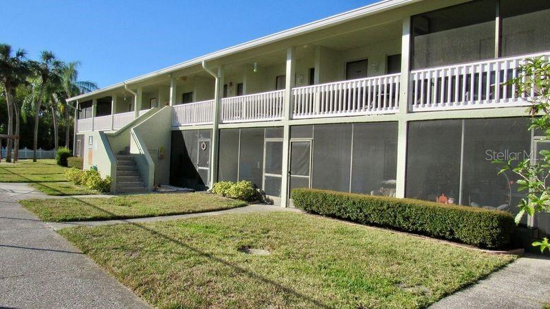 A two-story apartment building features a concrete staircase, screened-in ground-floor patios, and upper-level balconies — 20853 HAULOVER COVE UNIT A8, LUTZ, FL