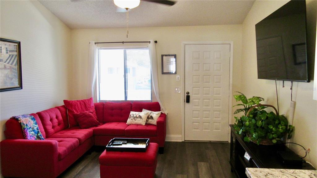 A living room features a red sectional sofa, a matching ottoman, and a wall-mounted television — 20853 HAULOVER COVE UNIT A8, LUTZ, FL