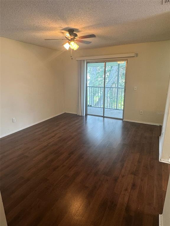 An empty room with dark wood-look flooring, a ceiling fan, and sliding glass balcony doors — 4227 PERSHING POINTE PLACE UNIT 8, ORLANDO, FL