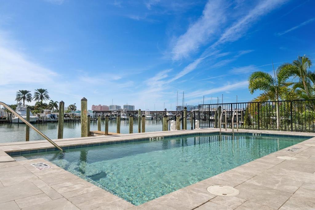 A rectangular swimming pool overlooks a marina with boats under a clear blue sky — 211 DOLPHIN POINT UNIT 401, CLEARWATER BEACH, FL