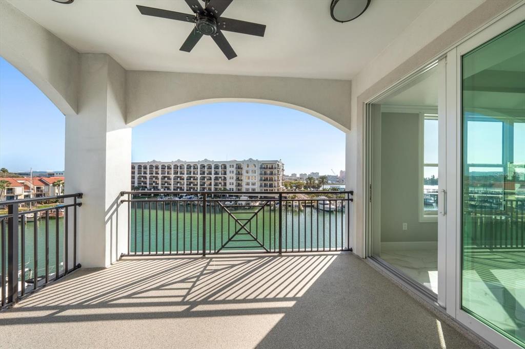 A covered balcony with a ceiling fan overlooks a canal and a large apartment building — 211 DOLPHIN POINT UNIT 401, CLEARWATER BEACH, FL