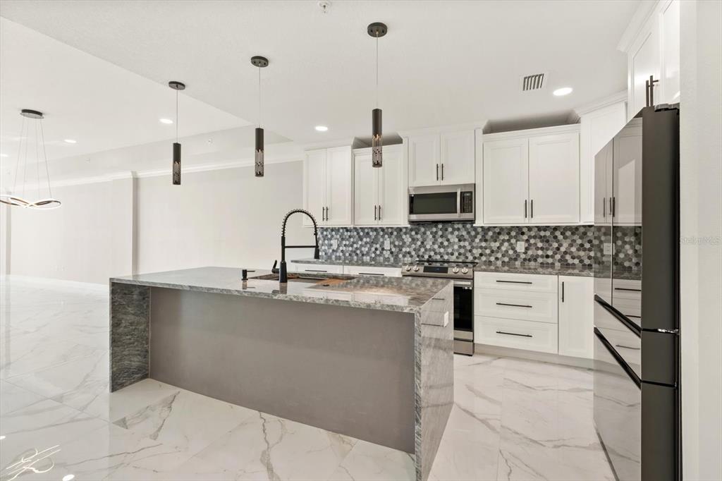 A modern kitchen features white cabinetry, a gray stone island, and a hexagonal tile backsplash — 211 DOLPHIN POINT UNIT 401, CLEARWATER BEACH, FL