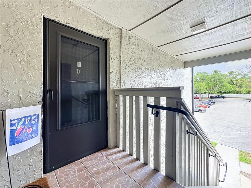 An exterior view of a building entrance with a dark storm door and stairs — 116 SPRINGWOOD CIRCLE UNIT D, LONGWOOD, FL