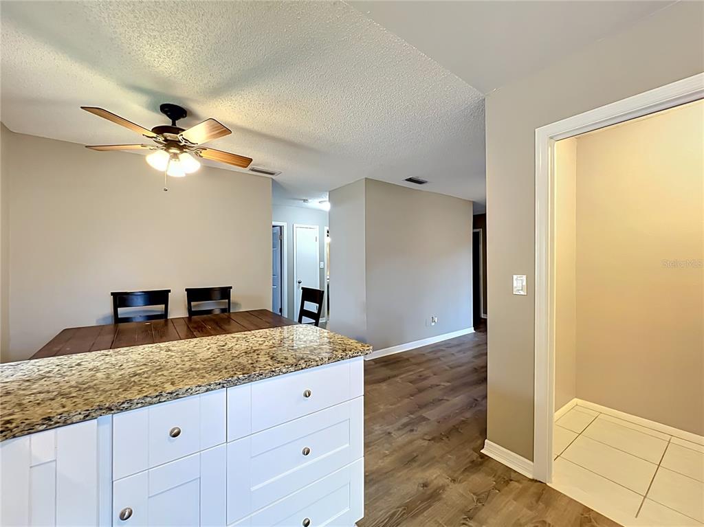 A kitchen island with granite countertops sits in front of a dining area and hallway — 116 SPRINGWOOD CIRCLE UNIT D, LONGWOOD, FL