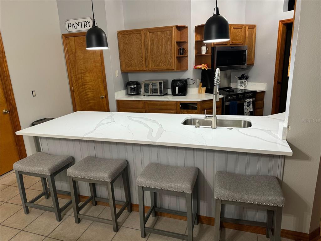 A kitchen features a white marble-look island with bar stools and wood cabinets — 1011 MINNESOTA AVENUE, ST CLOUD, FL