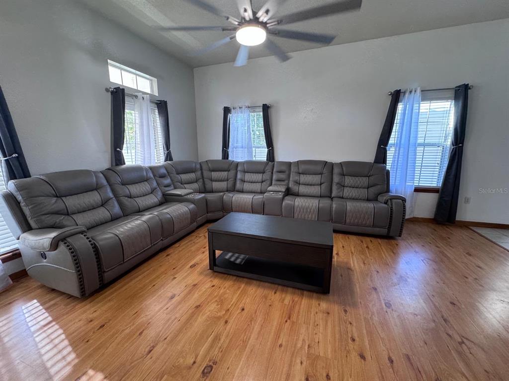 A living room features a large gray sectional sofa, a coffee table, and wood flooring — 1011 MINNESOTA AVENUE, ST CLOUD, FL