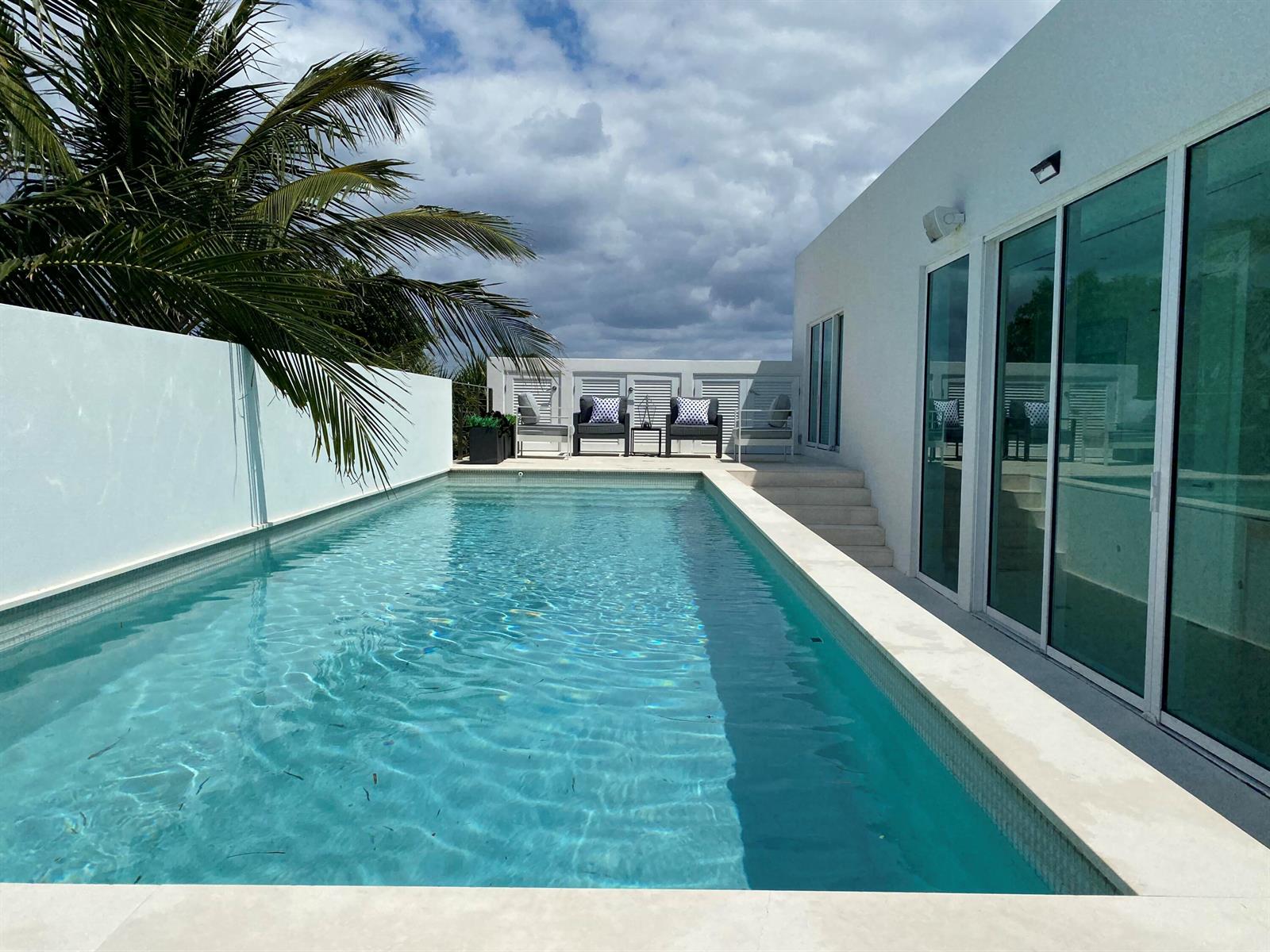 A rectangular swimming pool sits beside a modern white building with large glass sliding doors — 243 Venetian Drive, Delray Beach FL 33483, DELRAY BEACH, FL