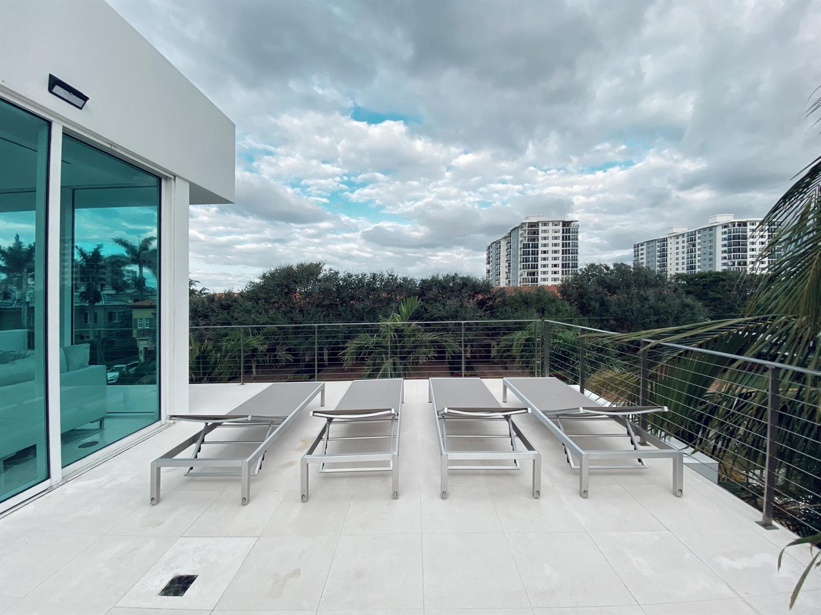 A rooftop terrace features four lounge chairs on white tile flooring with a metal railing — 243 Venetian Drive, Delray Beach FL 33483, DELRAY BEACH, FL