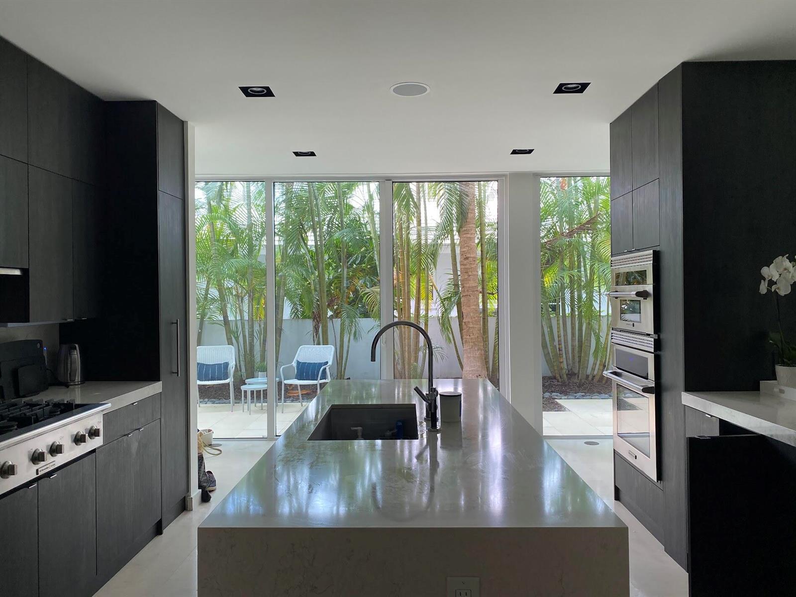 A modern kitchen with dark cabinetry, a large stone island, and floor-to-ceiling windows overlooking palms — 243 Venetian Drive, Delray Beach FL 33483, DELRAY BEACH, FL