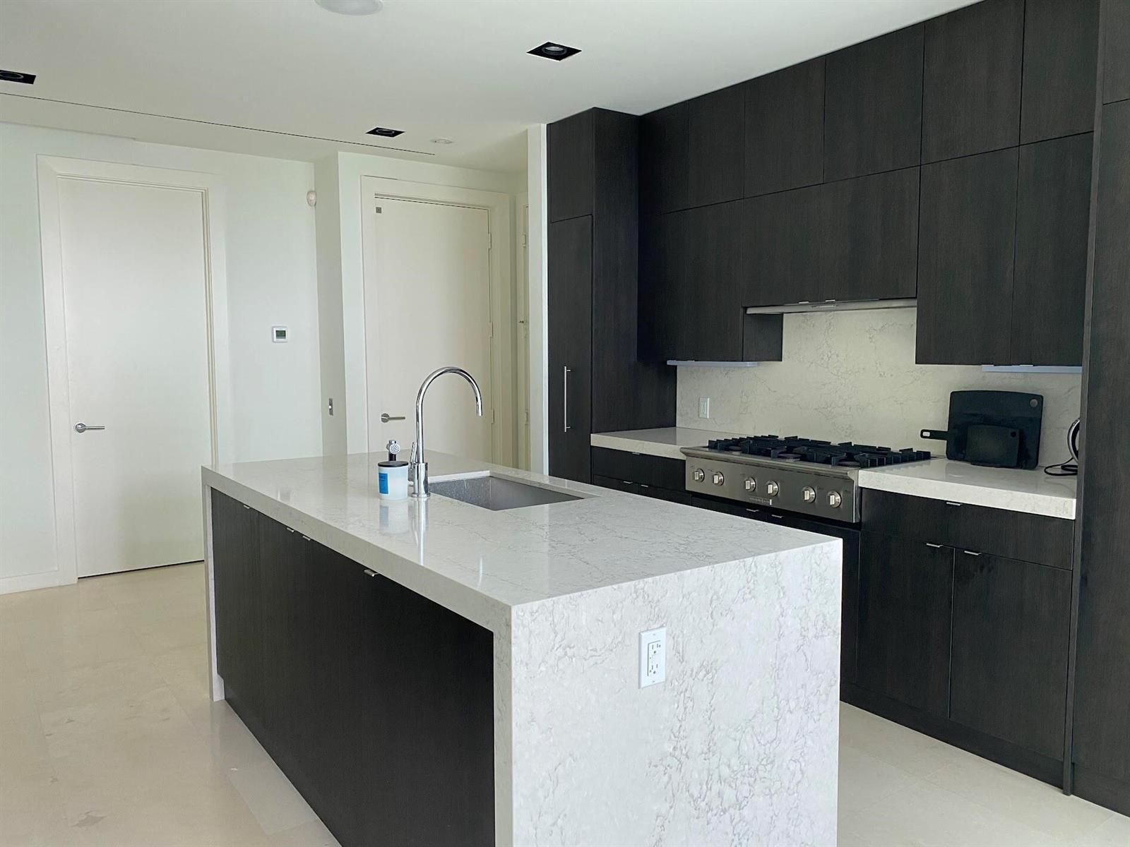 A modern kitchen features dark wood cabinetry, a white marble island, and stainless steel appliances — 243 Venetian Drive, Delray Beach FL 33483, DELRAY BEACH, FL