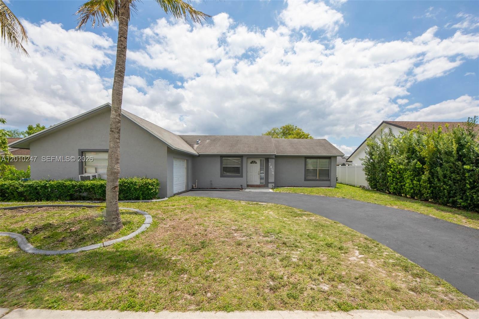 A single-story gray house features a curved driveway, a palm tree, and a front lawn — 7454 NW 48th Pl, Lauderhill FL 33319, LAUDERHILL, FL