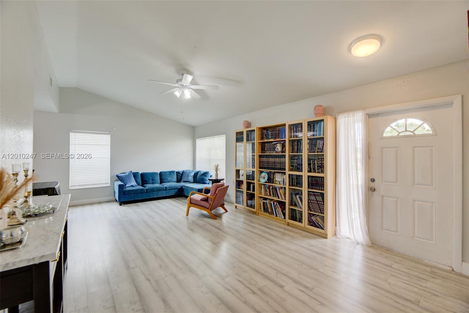 A living room features light wood-look flooring, a blue sectional sofa, and tall wooden bookshelves — 7454 NW 48th Pl, Lauderhill FL 33319, LAUDERHILL, FL