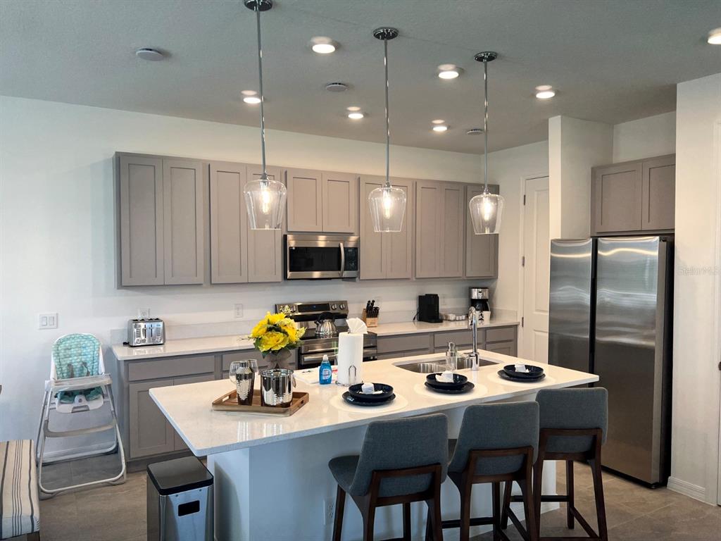 A kitchen features gray cabinets, a white quartz island with three stools, and stainless appliances — 955 CONCH ROAD, DAVENPORT, FL