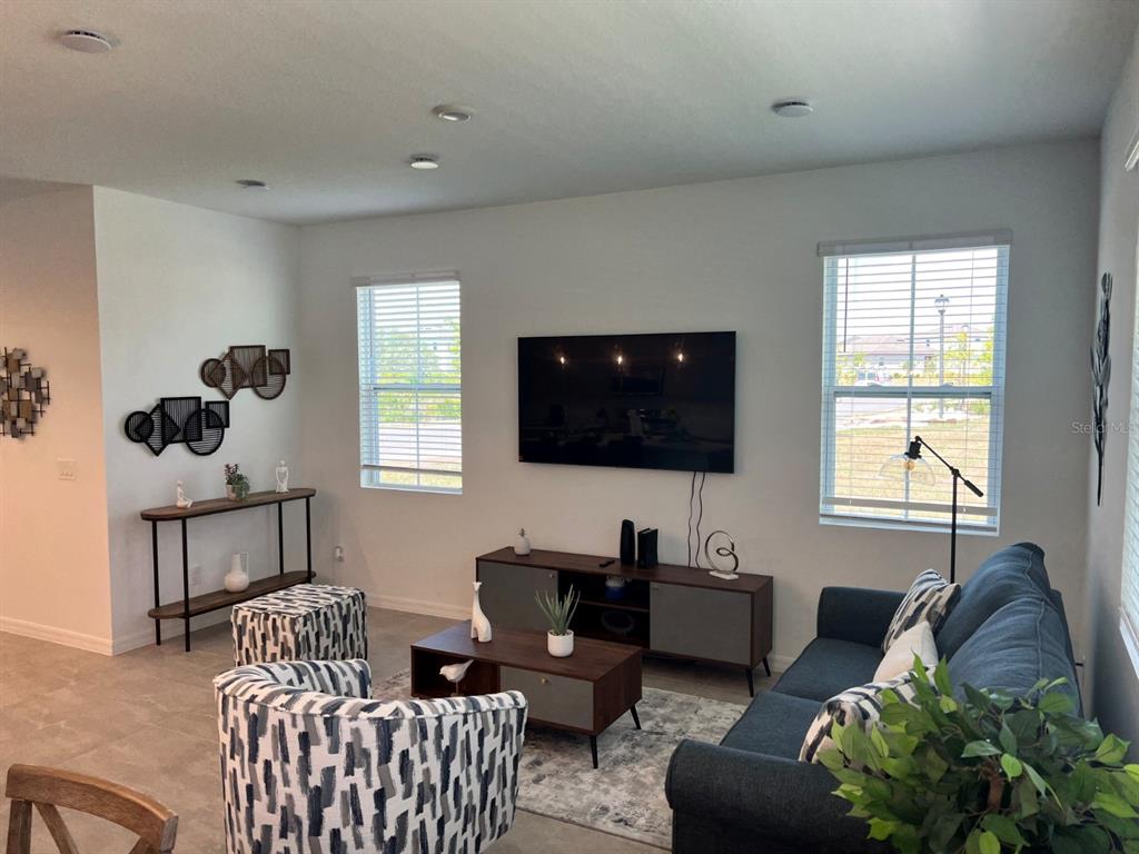 A living room features a wall-mounted television, a dark sofa, patterned chairs, and two windows — 955 CONCH ROAD, DAVENPORT, FL