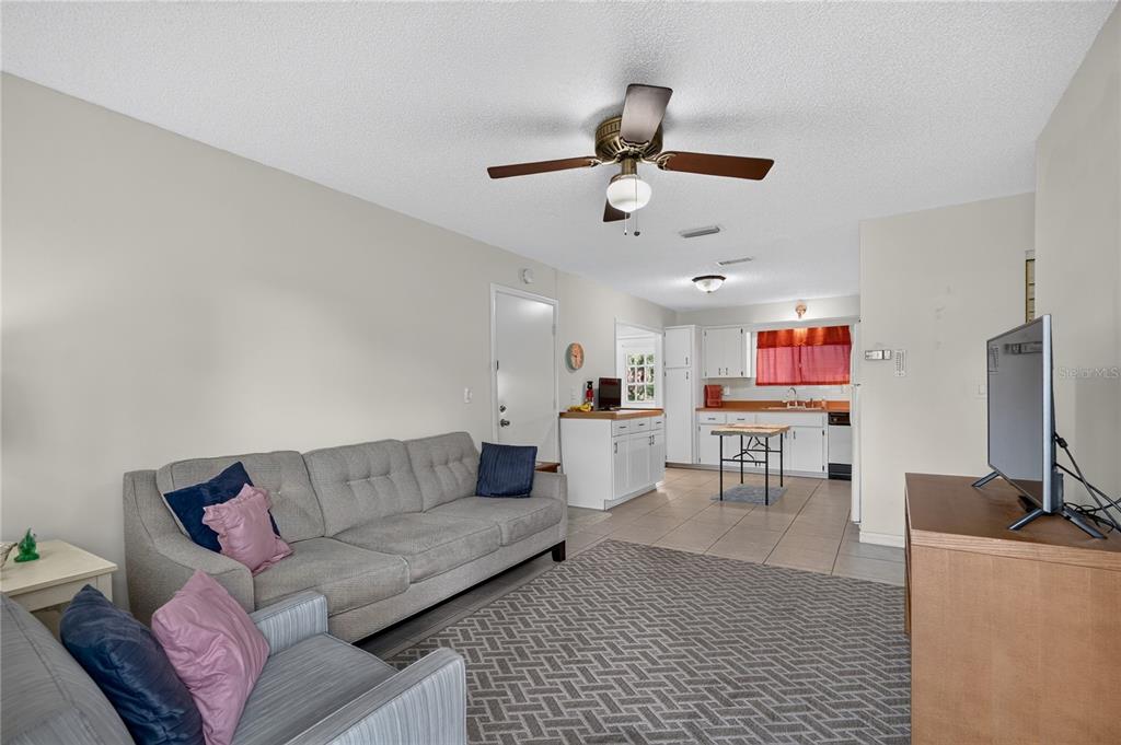 A living room with a grey sofa and armchair opens into a kitchen with white cabinets — 8392 SW 108TH LANE, OCALA, FL
