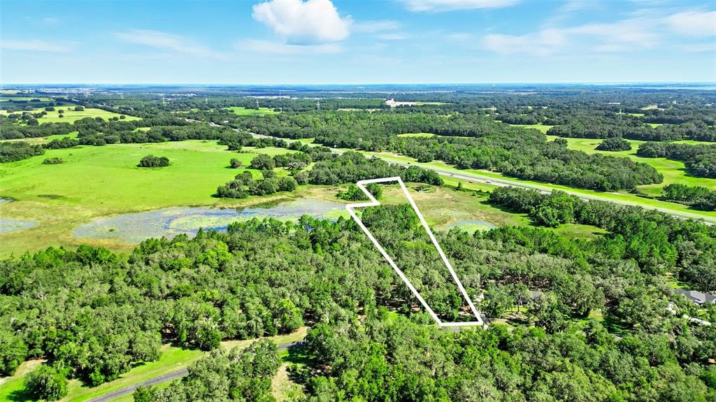 An aerial view shows a wooded lot outlined in white near a pond and highway — 3155 BRIGHT LAKE CIRCLE, GROVELAND, FL