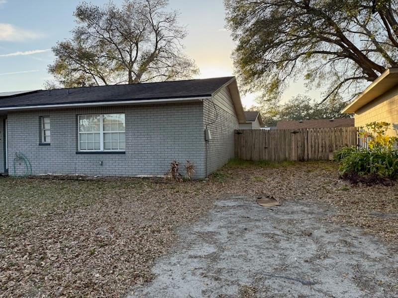 A gray brick house exterior with a gravel driveway and a wooden privacy fence — 4906 PRESIDENTIAL STREET, SEFFNER, FL