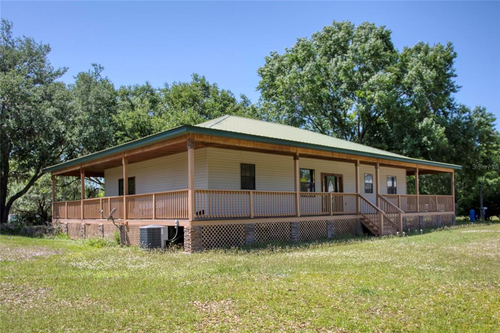 A single-story house with a wrap-around porch, metal roof, and lattice skirting on a lawn — 5525 MITCHELL BRIDGES ROAD, CLERMONT, FL