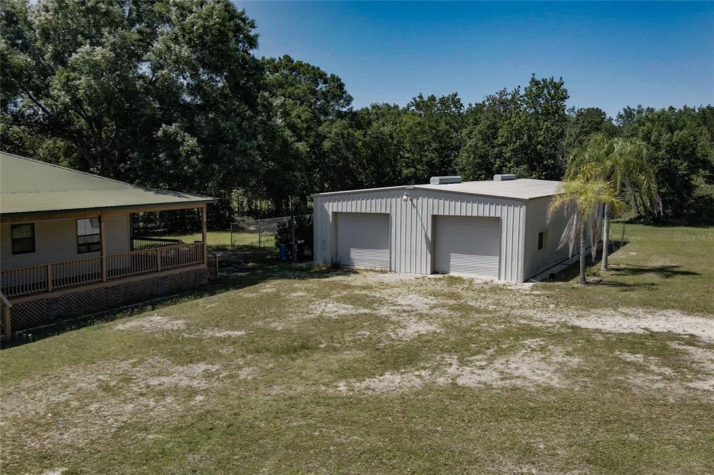 An exterior view shows a house with a porch next to a metal workshop building — 5525 MITCHELL BRIDGES ROAD, CLERMONT, FL