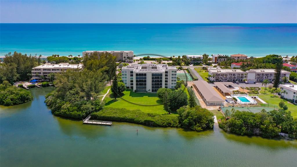 An aerial view shows a multi-story apartment building surrounded by green lawns and coastal water — 3240 GULF OF MEXICO DRIVE UNIT B303, LONGBOAT KEY, FL
