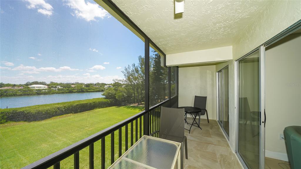 A screened-in balcony with tile flooring overlooks a grassy lawn and a body of water — 3240 GULF OF MEXICO DRIVE UNIT B303, LONGBOAT KEY, FL