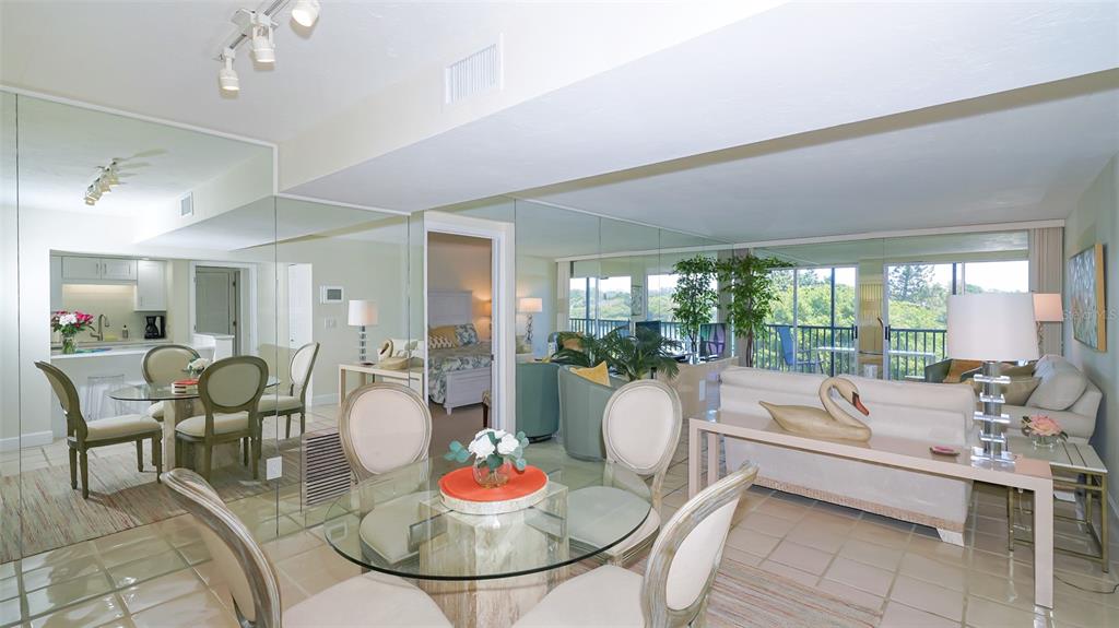 A dining area with a glass table and mirrored walls overlooks a living room and balcony — 3240 GULF OF MEXICO DRIVE UNIT B303, LONGBOAT KEY, FL