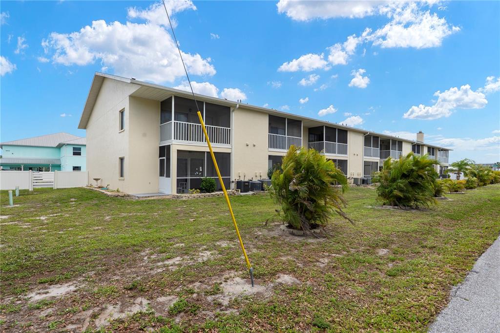 A two-story apartment building with screened balconies sits on a grassy lot — 22278 VICK STREET UNIT A112, PUNTA GORDA, FL