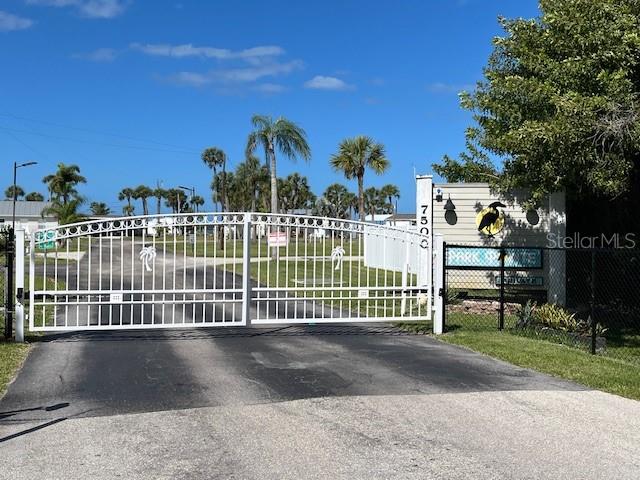 A white metal gate stands at the entrance of a property with palm trees — 7500 PARK POINTE DRIVE UNIT 42, ENGLEWOOD, FL
