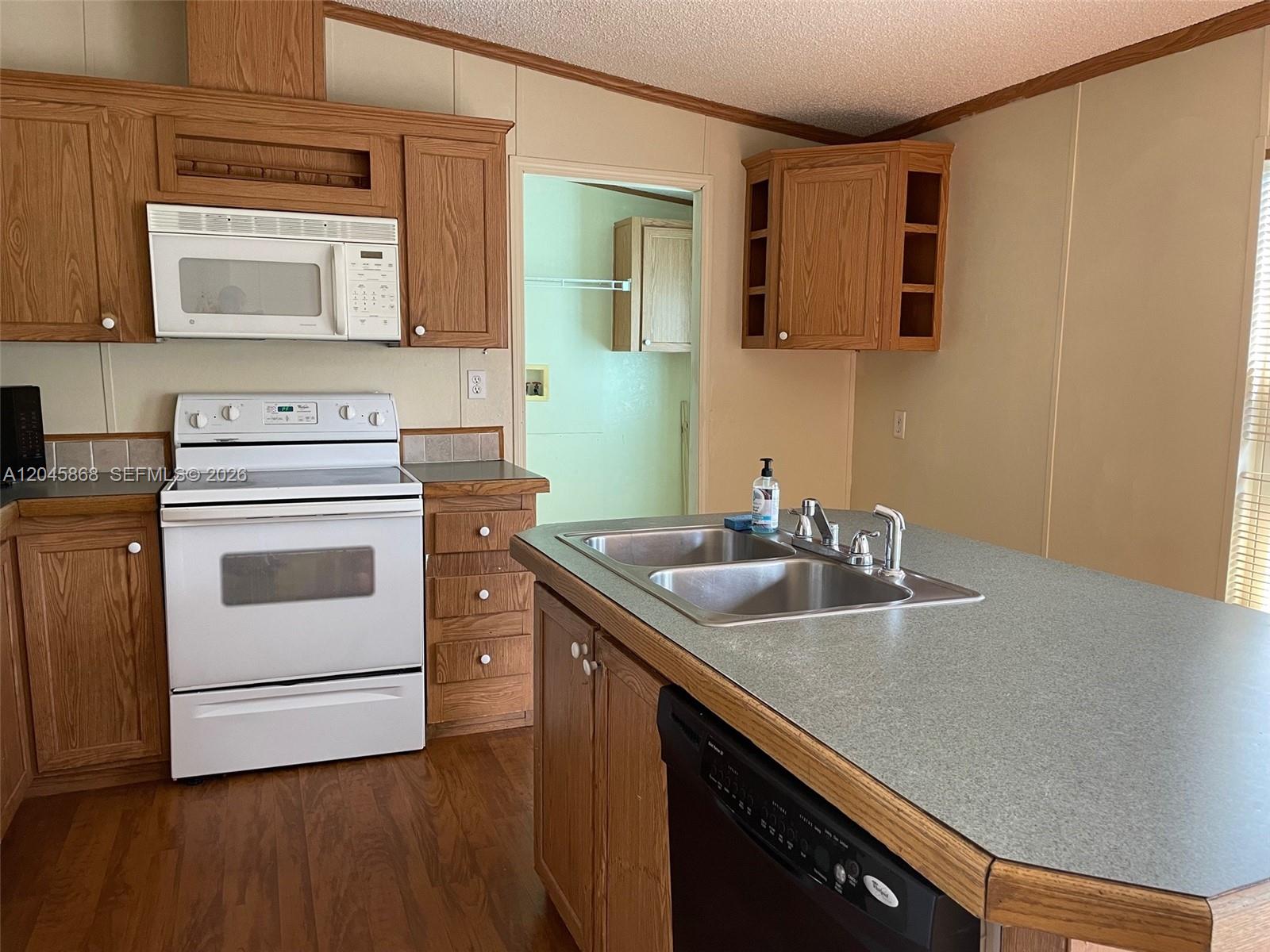 A kitchen features wood cabinets, white appliances, a center island with a sink, and laminate countertops — 11864 Atlantic Cir # H, Boca Raton FL 33428, BOCA RATON, FL