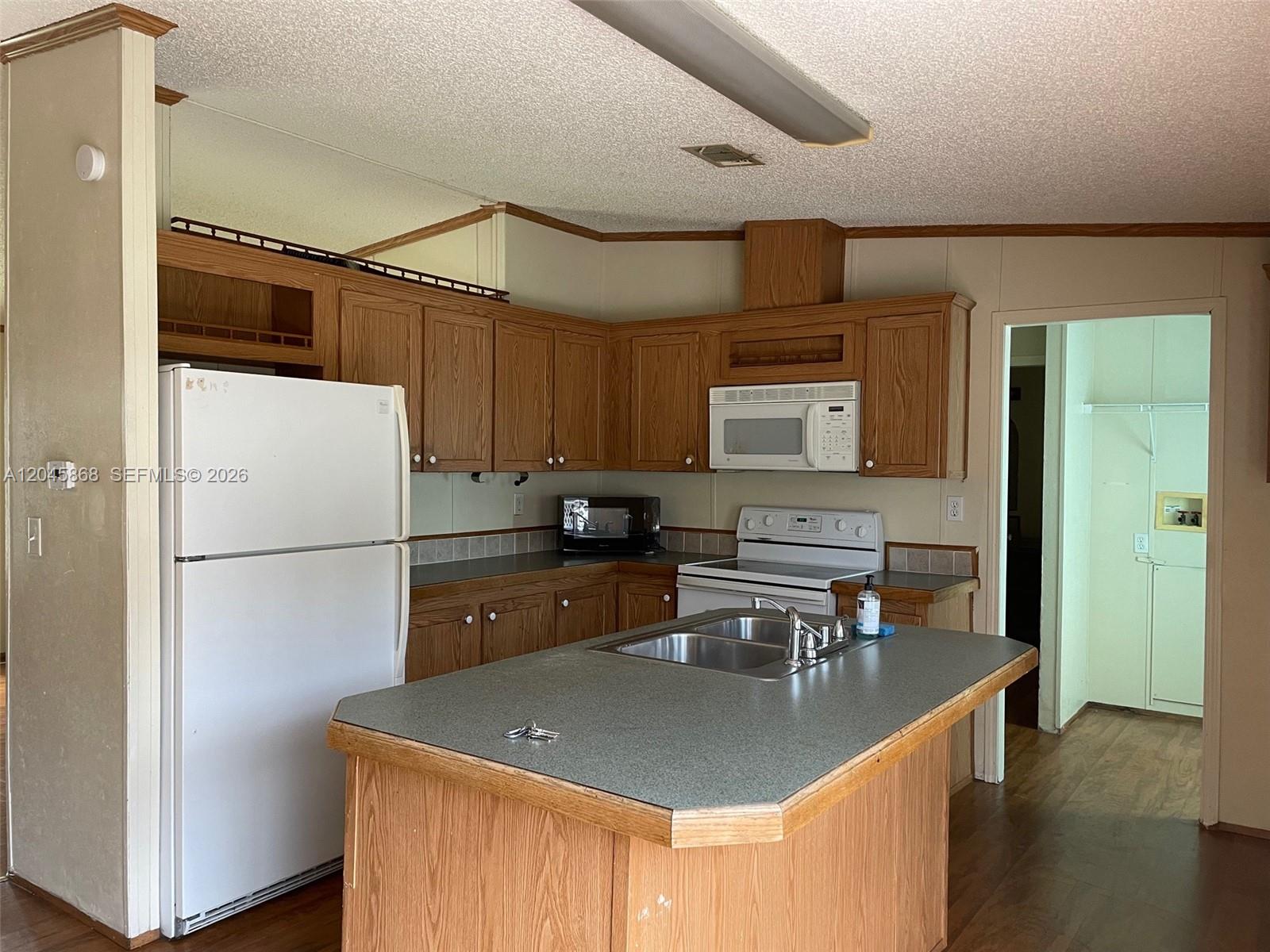 A kitchen features wood cabinets, a central island with a sink, and white appliances — 11864 Atlantic Cir # H, Boca Raton FL 33428, BOCA RATON, FL