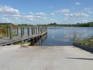A concrete boat ramp leads into a lake next to a wooden pier with pilings — 15785/15793/15801 HENNIPEN CIRCLE, PORT CHARLOTTE, FL