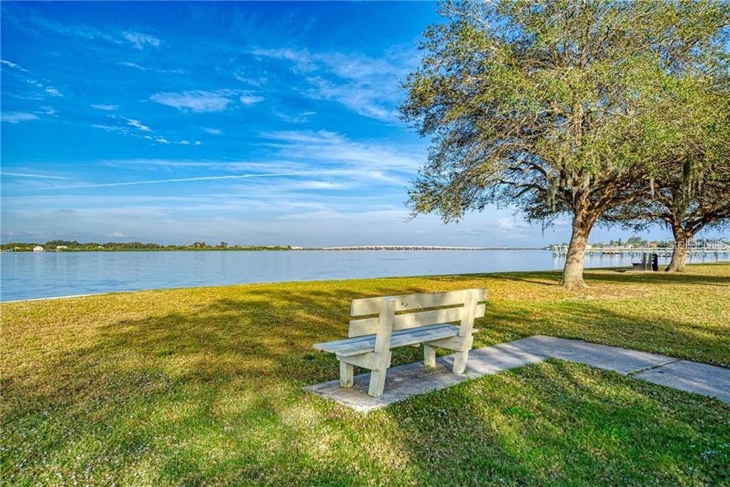 A wooden bench sits on a grassy lawn overlooking a large body of water — 15785/15793/15801 HENNIPEN CIRCLE, PORT CHARLOTTE, FL
