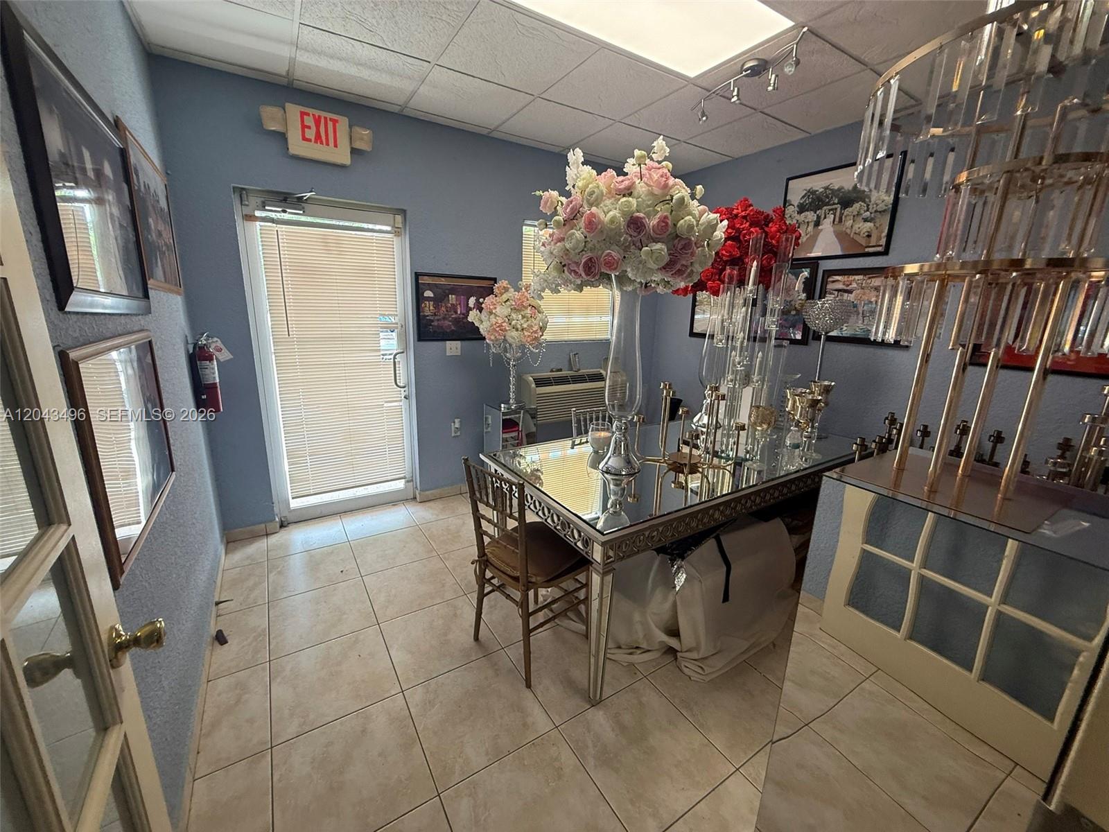 A small room features a mirrored table, floral centerpieces, and a glass door with blinds — 5921 NW 176th St # 9, Hialeah FL 33015, HIALEAH, FL