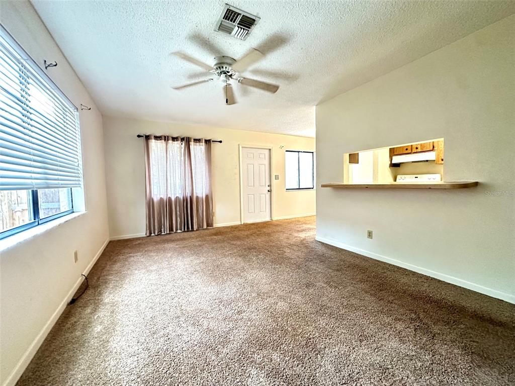 A carpeted living room features a ceiling fan, a window with blinds, and a kitchen pass-through — 3635 135TH AVENUE UNIT C, LARGO, FL