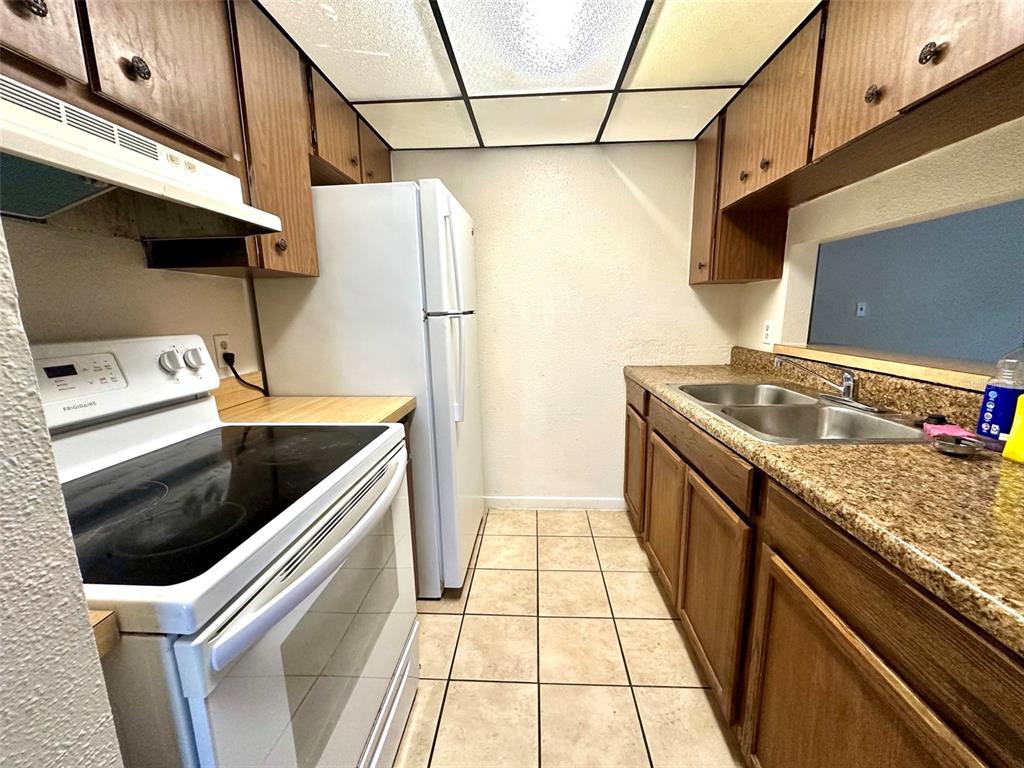 A galley kitchen features wood cabinets, granite countertops, tile flooring, and white appliances — 3635 135TH AVENUE UNIT C, LARGO, FL