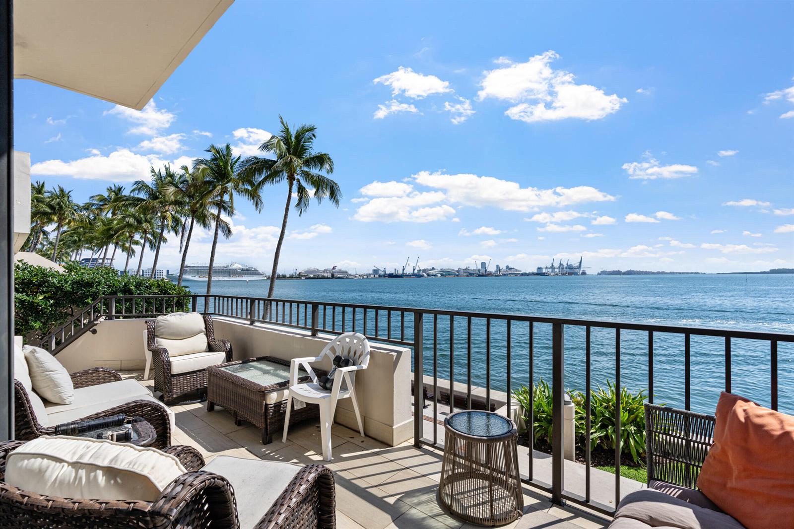 A balcony with wicker furniture overlooks a harbor with cruise ships and palm trees — 520 Brickell Key Drive # A200, Miami FL 33131, MIAMI, FL